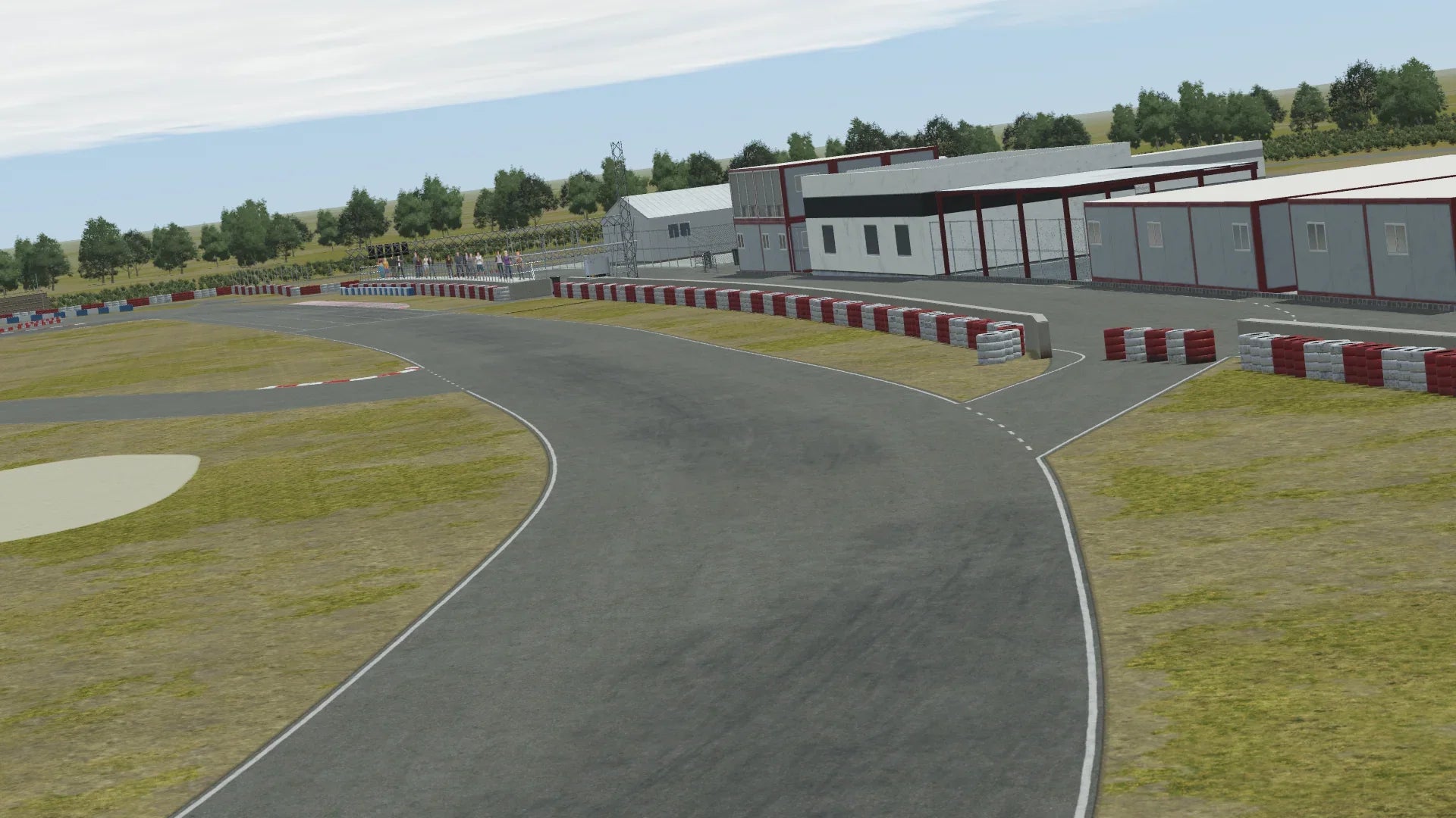 In-simulation view of the Valencia karting circuit pit complex in KartSim software, showing the asphalt track with red-white barriers, pit buildings, control tower, surrounding trees, and a partly cloudy sky.