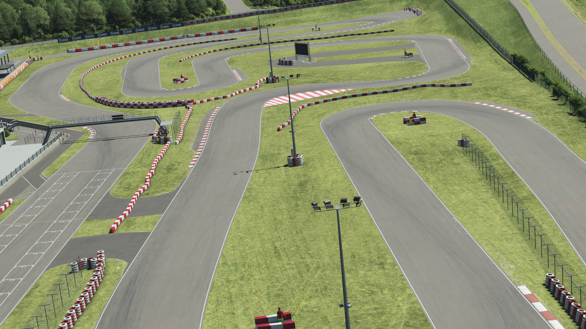 Panoramic in-simulation view of the Wackersdorf karting circuit in KartSim software, featuring multiple complex turns, red-white kerbs, grass run-off areas, spectator fencing, and paddock buildings under a sunny sky.