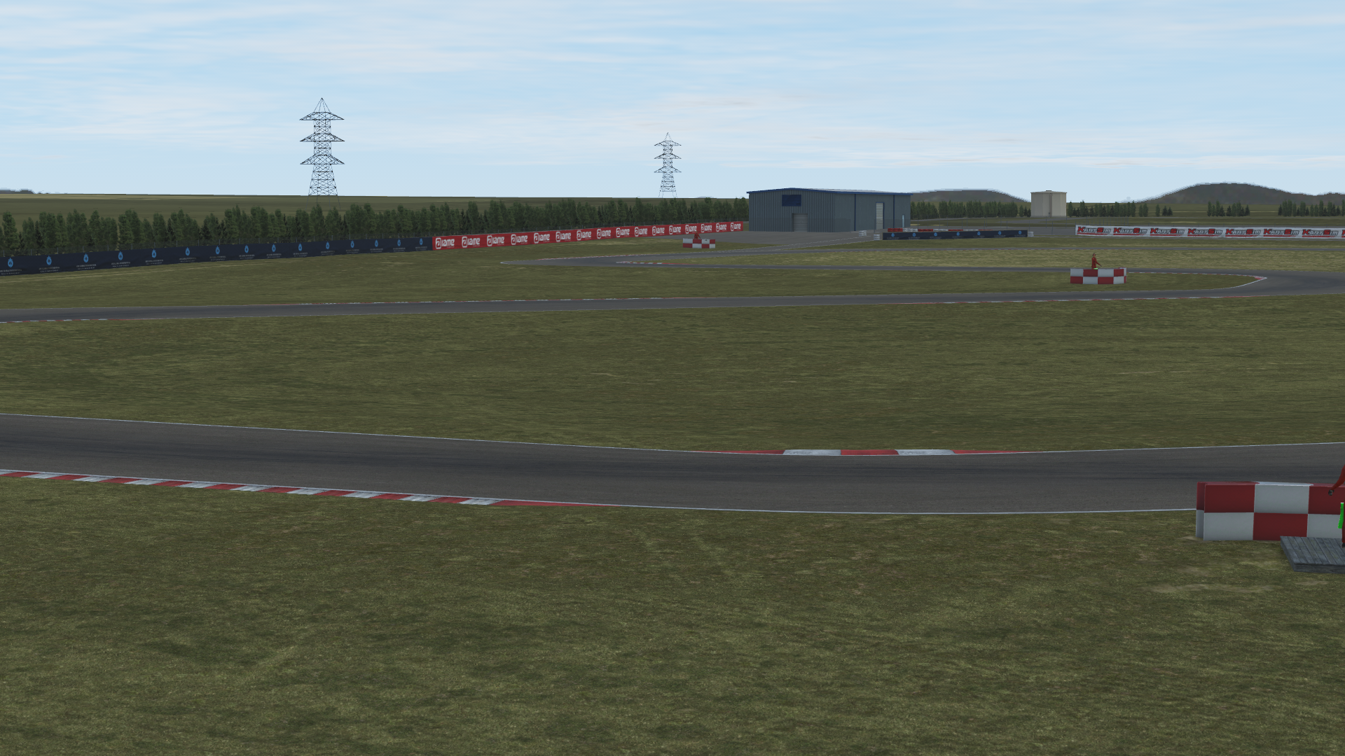 Panoramic in-simulation view of the Zuera karting circuit in KartSim software, showing the asphalt track with red-white curbs, grass run-off areas, barrier fencing, pit buildings, and clear sky above.