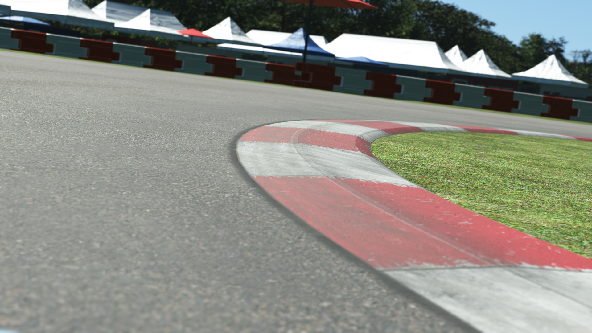 Close-up of MCC karting track curb – red and white corner detail with grassy edge and event tents in the background
