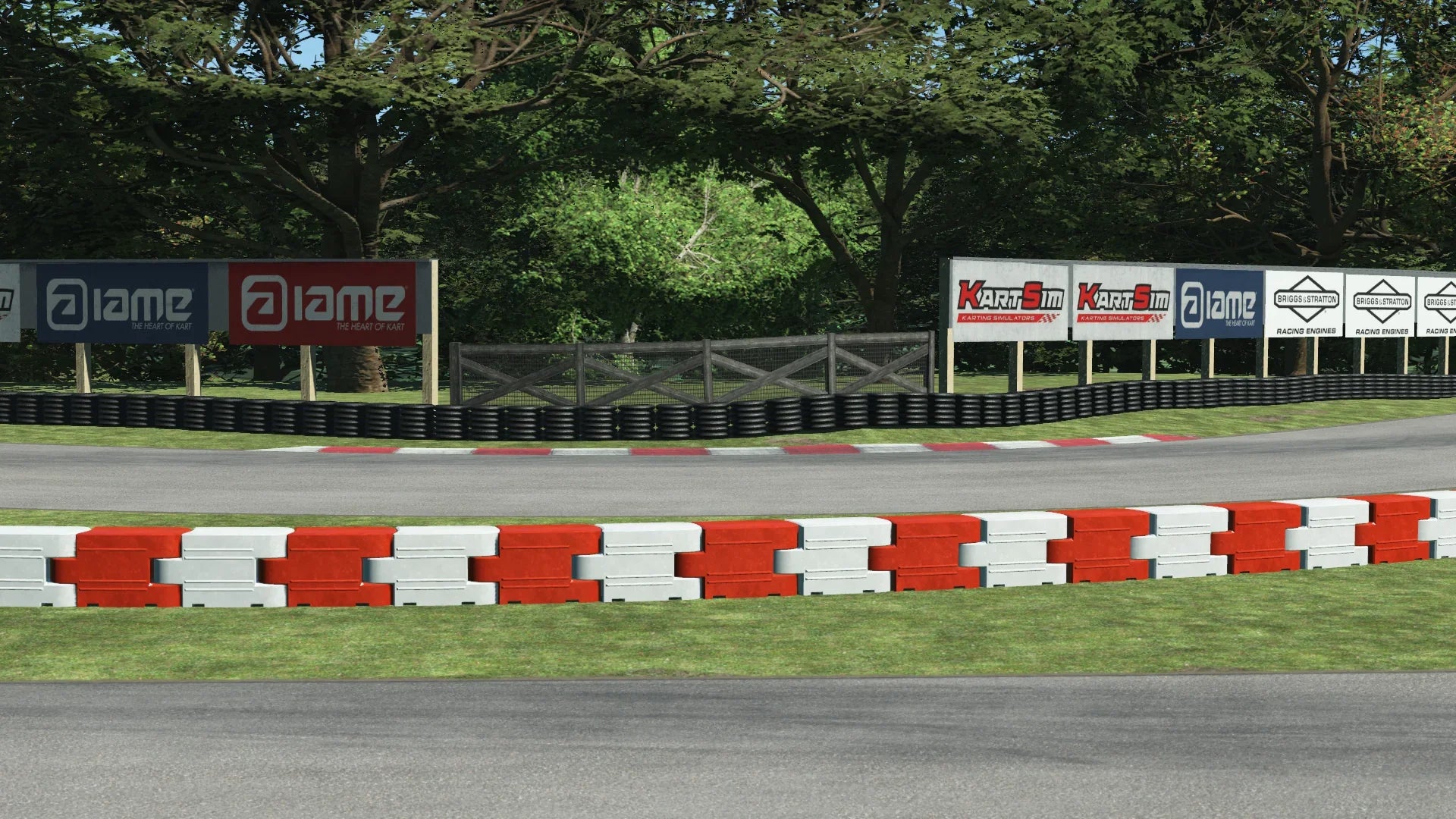 MCC karting trackside close-up – red and white safety barriers, tire wall, and branded sponsor boards with trees in the background
