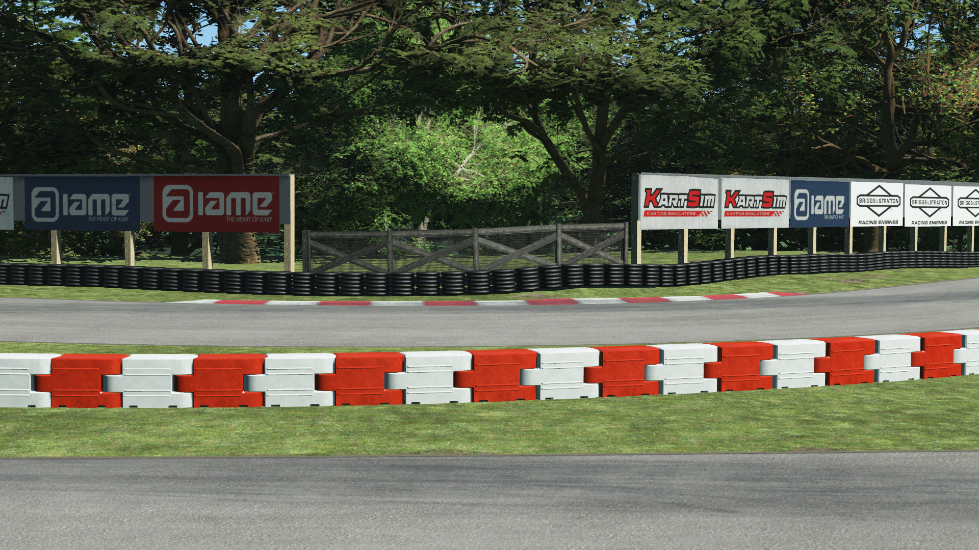 MCC karting trackside close-up – red and white safety barriers, tire wall, and branded sponsor boards with trees in the background