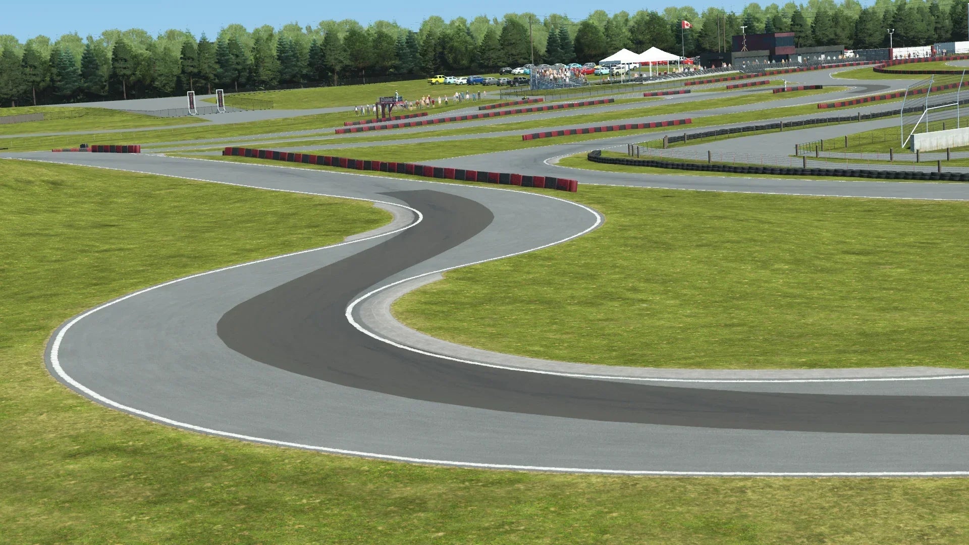 Winding section of Mosport karting track with red and black barriers, grassy terrain, and tree-lined background with spectators