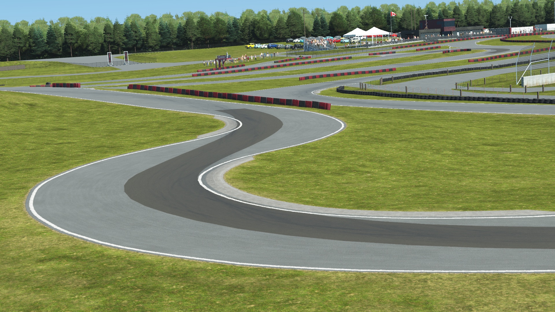 Winding section of Mosport karting track with red and black barriers, grassy terrain, and tree-lined background with spectators