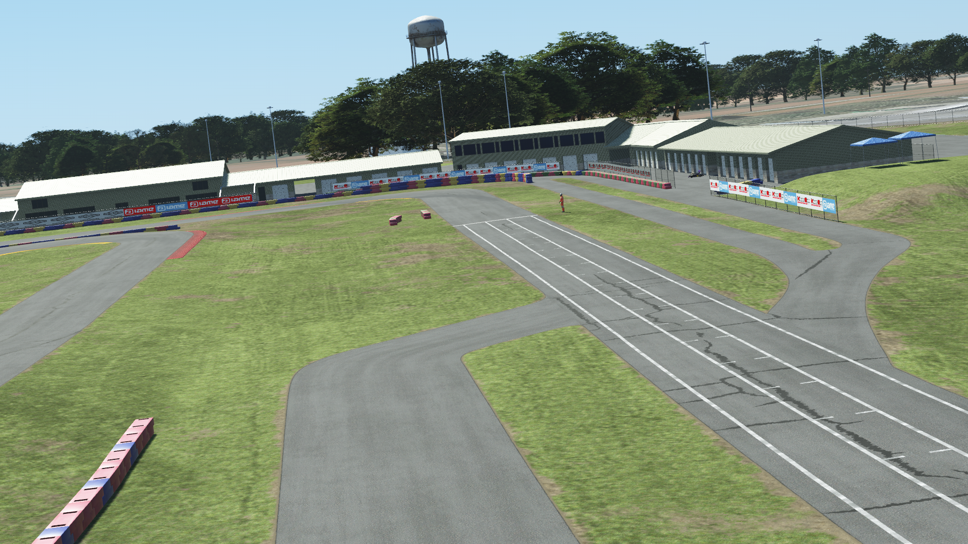 New Castle karting circuit with grid area, grass, barriers, and pit buildings under blue sky