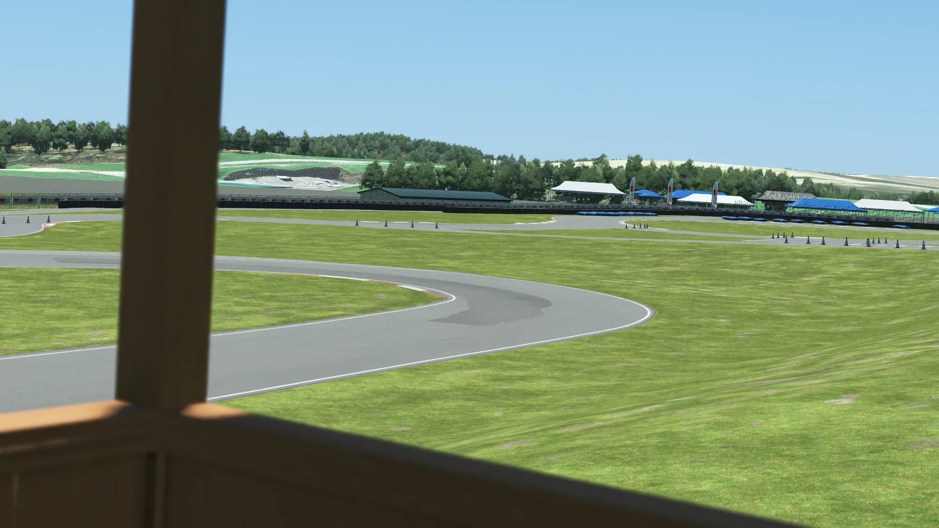 Trackside view of Pitt Race karting circuit from a wooden booth – corner section, grassy field, and spectator tents under clear sky