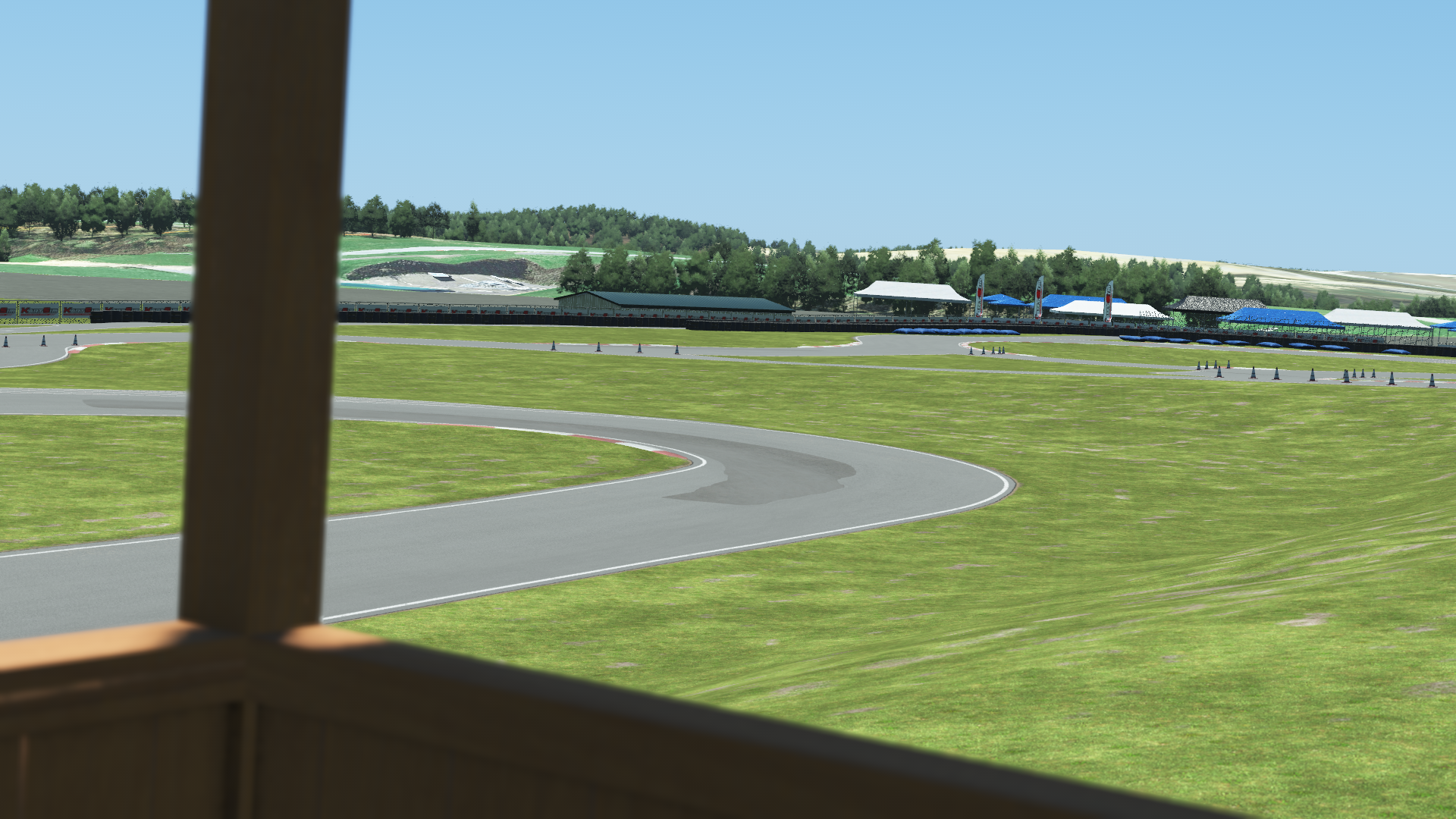Trackside view of Pitt Race karting circuit from a wooden booth – corner section, grassy field, and spectator tents under clear sky