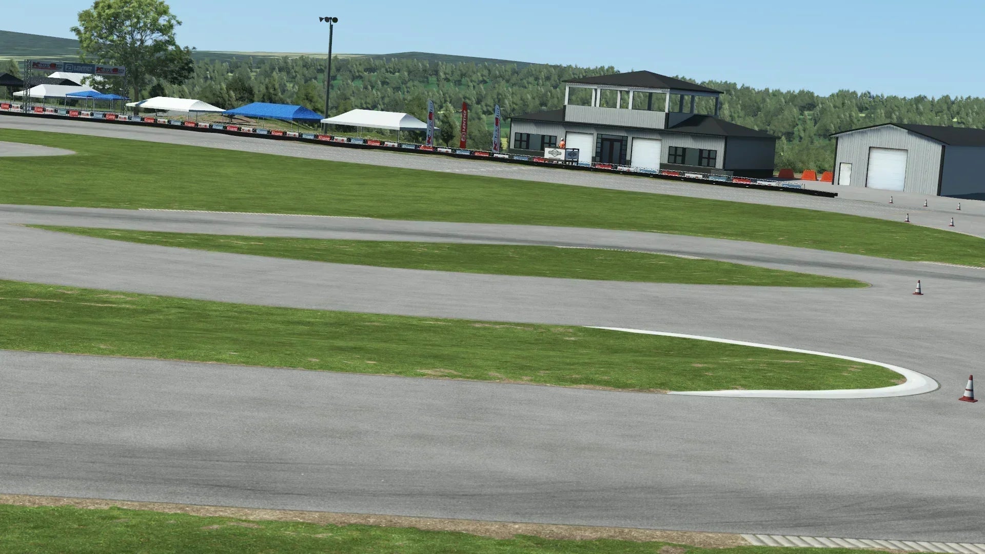 Karting race track with green grass, white tents, and paddock buildings in the background