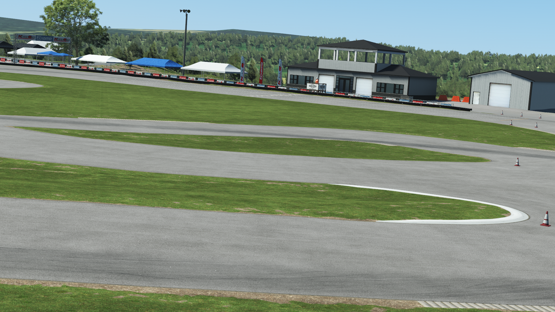 Karting race track with green grass, white tents, and paddock buildings in the background