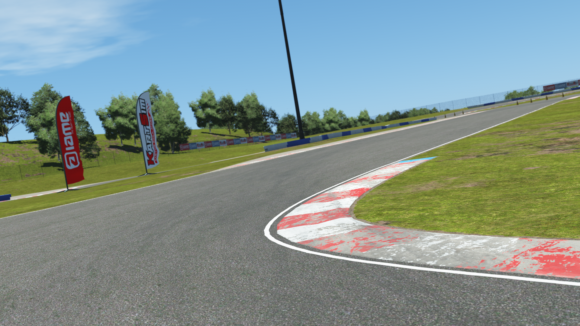 Trackside view of a karting corner with red and white curbs, sponsor flags, and a clear blue sky